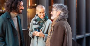 A trio of employees having a light-hearted conversation while standing outside together in cold weather attire.