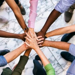 Overhead view of a group of employees putting their hands all together. They stand on a marble floor.