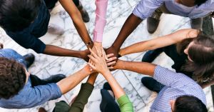 Overhead view of a group of employees putting their hands all together. They stand on a marble floor.