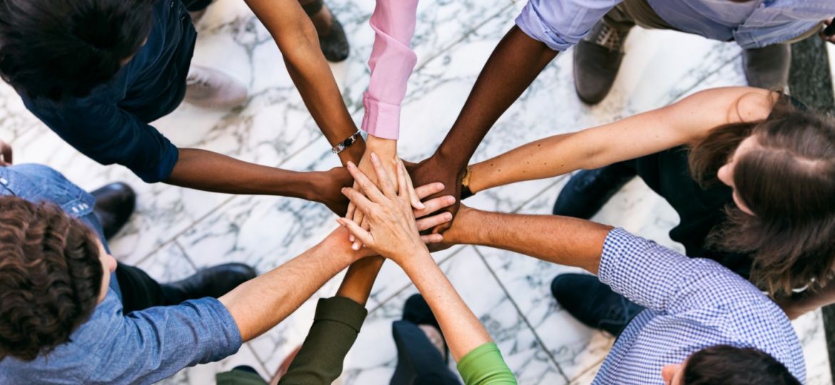 Overhead view of a group of employees putting their hands all together. They stand on a marble floor.